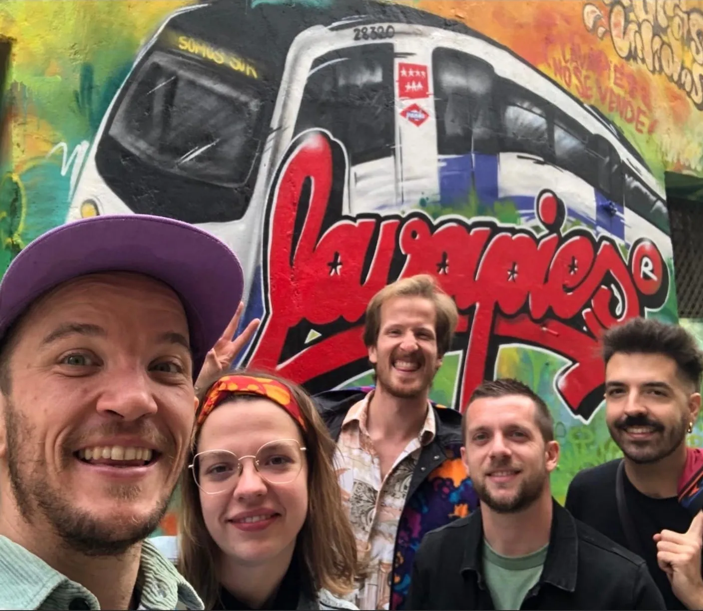 Lucas et quatre visiteurs souriants devant une fresque murale rouge représentant un métro et le mot Lavapiés