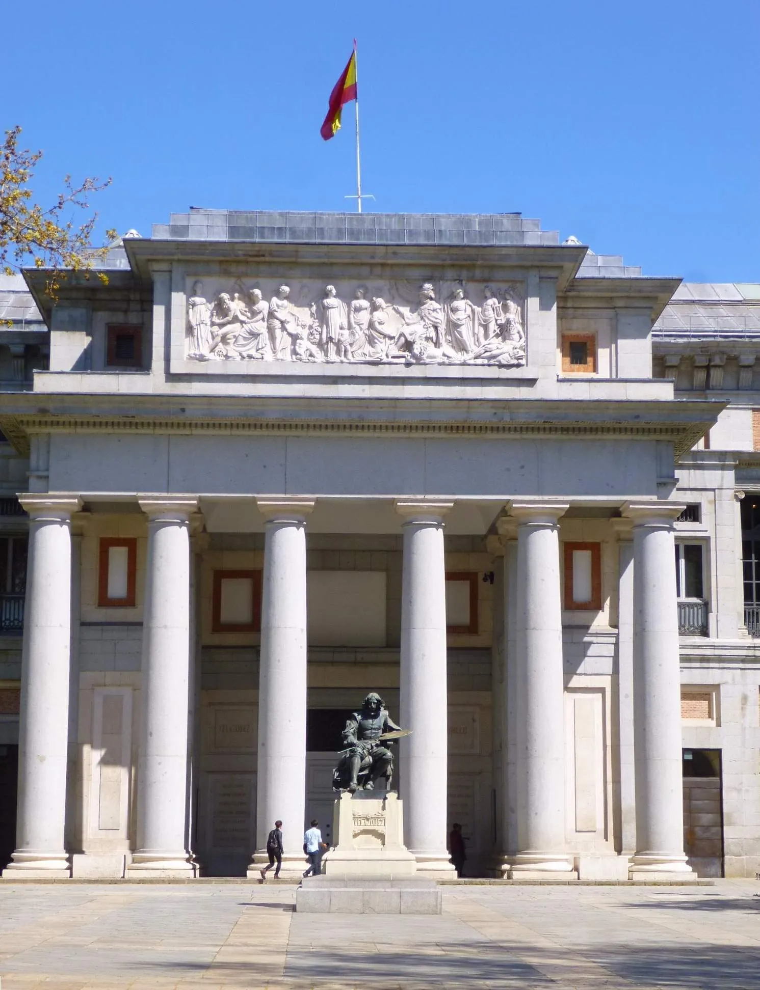 La façade néoclassique du musée du Prado, sa colonnade, le drapeau espagnol au-dessus du fronton et la statue de Velázquez devant l'entrée