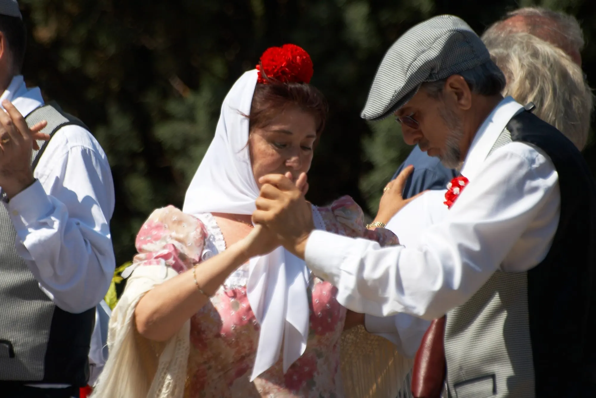 Un couple de chulapos danse le chotis pendant les fêtes de la San Isidro : elle en foulard blanc et œillet rouge dans les cheveux, lui en casquette pied-de-poule et gilet, un œillet à la boutonnière
