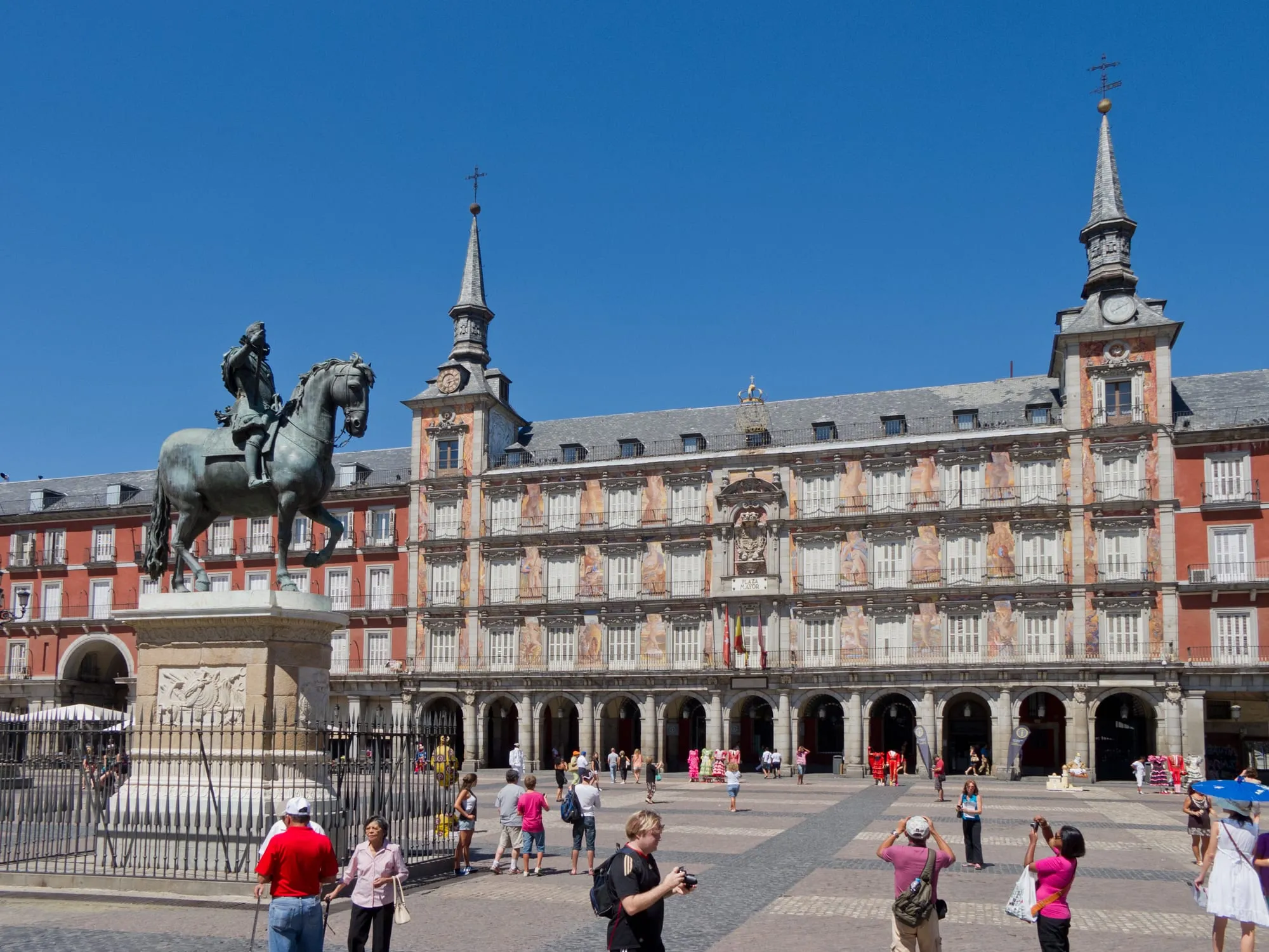 La statue équestre en bronze de Philippe III au centre de la Plaza Mayor de Madrid, devant la façade rouge et les deux flèches d'ardoise de la Casa de la Panadería, par ciel bleu