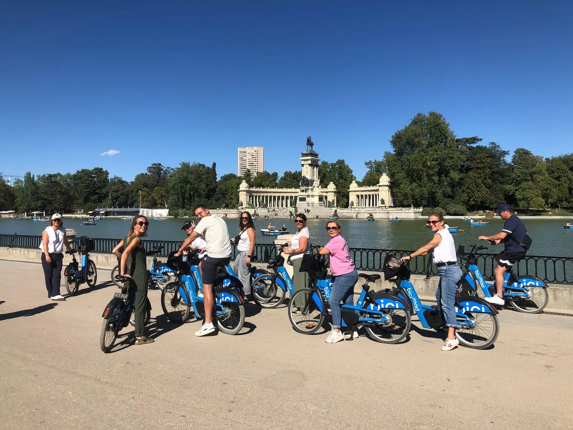 Un groupe à vélo BiciMAD posant au bord du grand bassin du Retiro, le monument à Alphonse XII en arrière-plan sous un ciel bleu